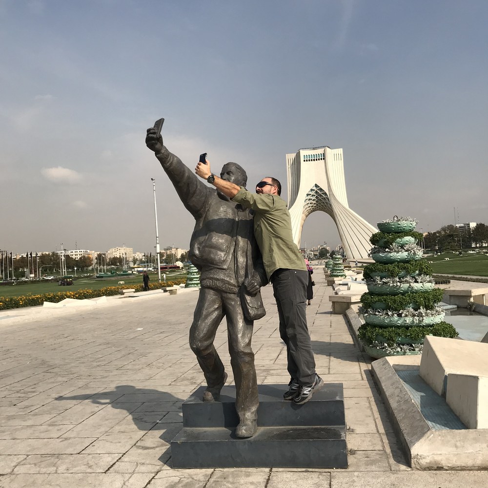 Zdjęcie z pomnikiem robiącym selfie, w tle wieża Azadi w Teheranie