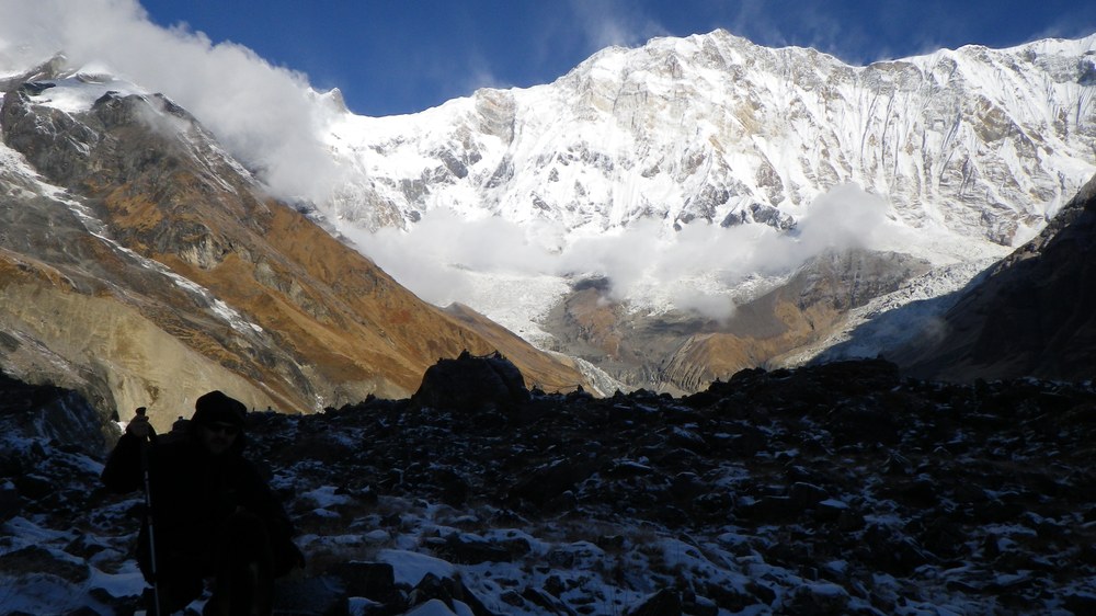 Lodowcowa ściana Annapurny nad moreną, w dole sylwetki trekkerów