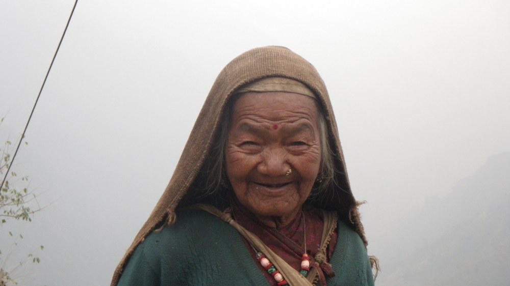 Portret starszej Nepalki w chuście, we mgle nad doliną