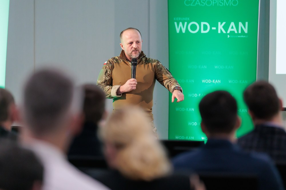 Wystąpienie z mikrofonem przed ścianką konferencji branżowej WOD-KAN